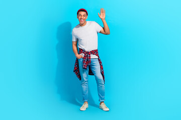 Full size photo of satisfied glad young person put arm pocket palm waving hello isolated on blue color background © deagreez