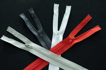White, red, black and gray zipper on black background. Fabric, textile, fashion clothes, garment,...