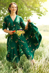 a young girl in a green dress,with a bouquet of flowers,stands in the wind in a field,the wind...