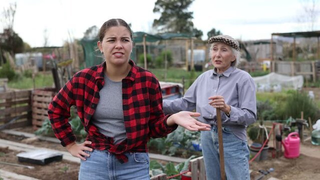 Two angry casual women neighbors of different ages arguing during the vegetable garden season on sunny day of spring
