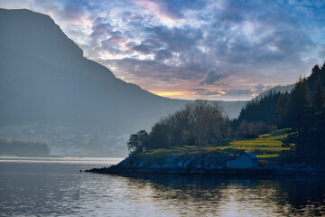 Sunset on the fjord with mountains in Norway. Diffuse light, sun rays on a meadow