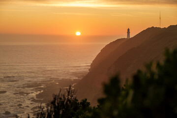 Sunset view on the coast with lighthouse standing on the cliff in the distance, ocean, orange sky and backlit at the great ocean road, Victoria, Australia 