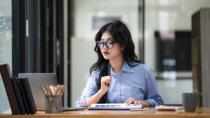 An attractive Asian businesswoman wearing eyeglasses thoughtful thinking about work in a new project.
