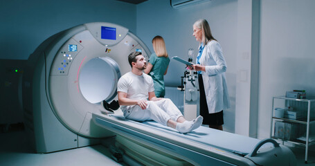 Male patient is waiting to be scanned. Man have talk with female doctor. Nurse is preparing for performing of magnetic resonance tomography. Patient is getting ready for MRI examining. - obrazy, fototapety, plakaty