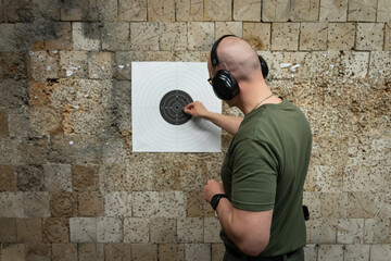 A male shooter near a paper target in a shooting range.