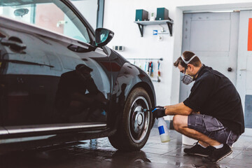 Service man washing car before detailing in workshop.