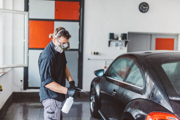Service man washing car before detailing in workshop.