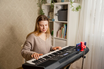 Teacher teaching her student to play piano and recording lesson online. Young pretty woman at home playing on synthesizer for followers, live streaming concert. Online education and leisure concept.