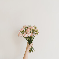 Female hand holding beautiful carnation flowers bouquet. Flat lay, top view. Elegant floral composition