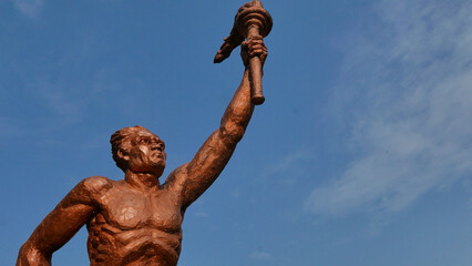 Surakarta, Indonesia, 20th June 2023, Statue of spirit of sport in a form of man holding torch against blue sky, Patung obor manahan located at the Manahan stadium Surakarta