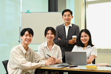 Group of company employees sitting in modern office and smiling confidently to camera