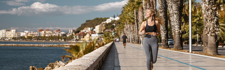 Fototapeta na wymiar Sporty female jogging on sidewalk along seashore