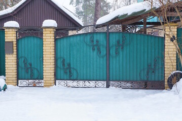 a large closed metal green gate and a closed iron door with a black forged pattern in a snowdrift...