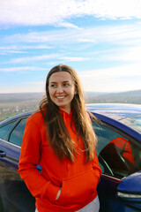 A woman stands near the car.Girl with a auto.Woman driver.Woman auto enthusiast.Driving a car as a hobby.Renting a car.The girl has long hair.The wind blows hair. car rent.driving school. happy girl.