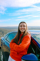 A woman stands near the car.Girl with a car.Woman driver.Woman auto enthusiast.Driving a car as a hobby.Renting a car.The auto stands in nature.The girl has long hair.Driving school.Rent a auto.travel