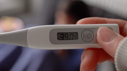 Close-up view of a thermometer showing a high temperature against a blurry background of a child