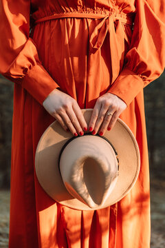 Junge Frau in oranger Kleid hält in den Händen ein Hut in Country-Stil