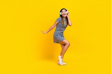 Fototapeta na wymiar Full length photo of funky cheerful lady wear striped dress dancing listening songs empty space isolated yellow color background