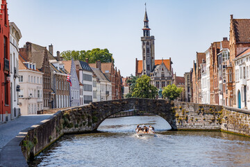 Naklejka premium Stone bridge across the Langerei Canal in Bruges, with a tourist boat passing below the bridge, Brugge, Belgium