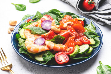 Fresh salad for keto diet with shrimp, salmon, avocado, spinach, cucumber, tomato, cashew nuts, sesame. Low-carbohydrate lunch rich in healthy fats. White table background, top view