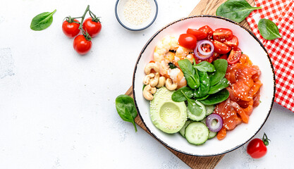 Keto salad with spinach, salmon, shrimp, avocado, cucumber, tomato, nuts, sesame seeds. Low-carbohydrate lunch rich in healthy fats. White table background, top view
