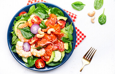 Fresh salad for keto diet with shrimp, salmon, avocado, spinach, cucumber, tomato, cashew nuts, sesame. Low-carbohydrate lunch rich in healthy fats. White table background, top view