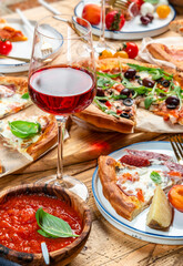 Pizza party dinner table. Glasses with red wine and plates, rustic wooden table with hot pizzas, italian appetizers, salads, cheese, fruits and berries. Family lunch with fast food