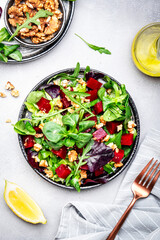 Beet salad with arugula, lettuce, chard and walnuts and lemon dressing, gray kitchen table, copy space. Fresh useful vegan dish for healthy eating