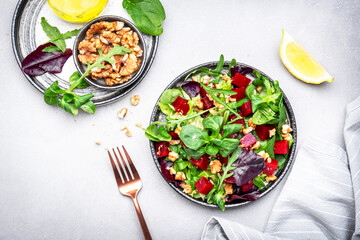 Beet salad with arugula, lettuce, chard and walnuts and lemon dressing, gray kitchen table, copy space. Fresh useful vegan dish for healthy eating