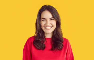 Obraz premium Full-face shot of beautiful young brunette girl in red sweater looking into the camera with happy, funny expression on her face. Studio portrait of happy young woman on isolated yellow background.
