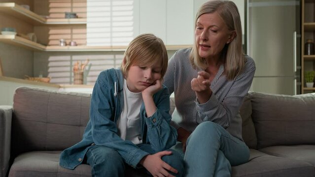Worried strict mature caucasian woman grandmother scolding lazy child grandson demand discipline angry senior female grandma punishing disobedient grandchild boy scold kid bad behavior couch at home