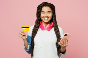 Young happy woman wear white sweatshirt casual clothes using mobile cell phone hold credit bank card doing online shopping order delivery booking tour isolated on plain pastel light pink background.