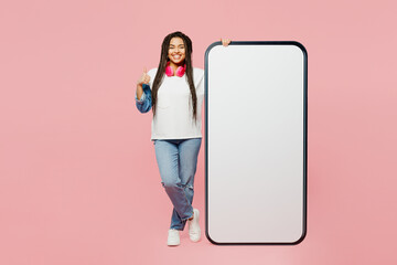 Full body fun young woman of African American ethnicity wear white casual clothes big huge blank screen mobile cell phone smartphone with area show thumb up gesture isolated on plain pink background.