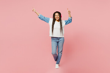 Full body woman of African American ethnicity in white sweatshirt casual clothes headphones listen to music look aside on area isolated on plain pastel light pink background studio Lifestyle concept