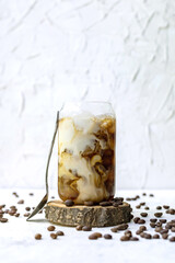 Glass of ice coffee with cream being poured into it showing the texture of drink on white