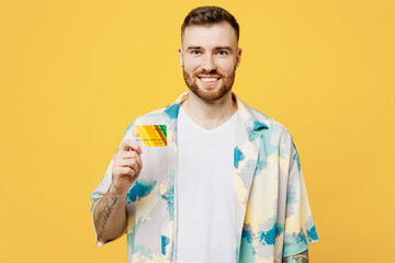 Young smiling happy man he wear blue shirt white t-shirt casual clothes hold in hand mock up of credit bank card isolated on plain yellow background studio portrait. Tattoo translates life is fight.