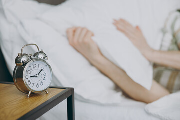 Close up cropped photo shot young man wearing casual clothes pajama lying in bed near clock alarm resting relax spend time in bedroom home in own room hotel wake up dream be in reverie good mood day.