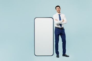 Full body young employee IT business man corporate lawyer wear classic formal shirt tie work in office stand near big huge blank screen mobile cell phone with area isolated on plain blue background.