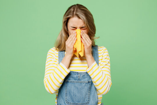 Sick unhealthy ill allergic woman has red watery eyes runny stuffy sore nose suffer from allergy trigger symptom hay fever cover mouth sneeze isolated on plain pastel green background studio portrait