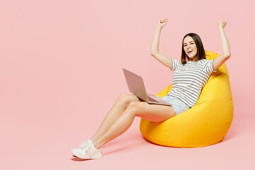 Full body young IT woman wears casual clothes t-shirt sit in bag chair hold use work on laptop pc...