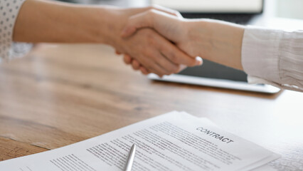 Business people shaking hands above contract papers just signed on the wooden table, close up. Lawyers at work. Partnership, success concept