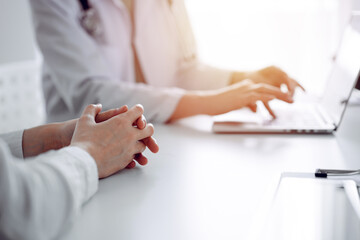 Doctor and patient discussing current health examination while sitting at the desk in clinic office. The focus is on female patient's hands, close up. Perfect medical service and medicine concept