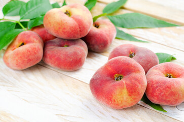 Fototapeta na wymiar Fresh Flat Peaches, Chinese Saturn Donut Peaches with Leaves on Wooden Bright Background