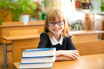 Back to school and happy time. Cute industrious child is sitting at a desk indoors. Kid is learning in classroom. Girl reading the book.