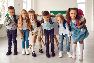 Group of happy children huddling in the classroom. Team of cheerful adorable friends with backpacks...