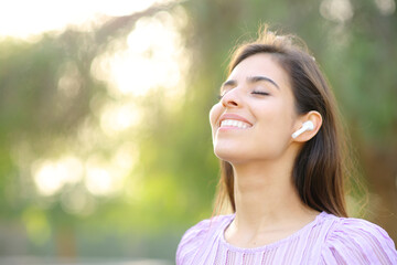 Happy woman breathing fresh air wearing earbud
