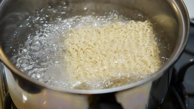 Adding a brick of ramen noodle to a pot of boiling water