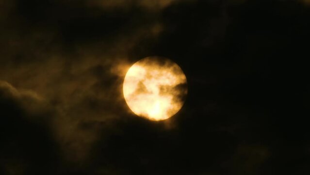 Radiant orange moon in night sky as dark clouds move. Static close-up shot