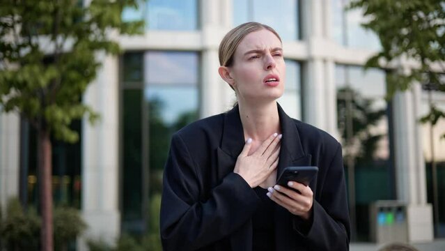 Businesswoman reading bad news and feels bad having breathing problems, chest pain, panic attack outdoors. Business woman female manager touches chest. Heart attack, thoracic osteochondrosis, asthma.