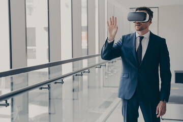 Excited businessman in VR glasses managing project in virtual reality, touching objects, office environment